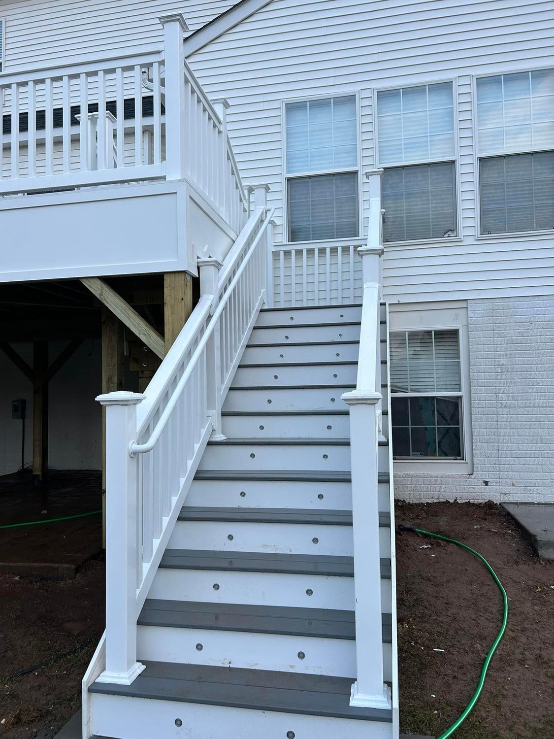 White deck stairs with gray treads lead to a deck. White railing, exterior of house.