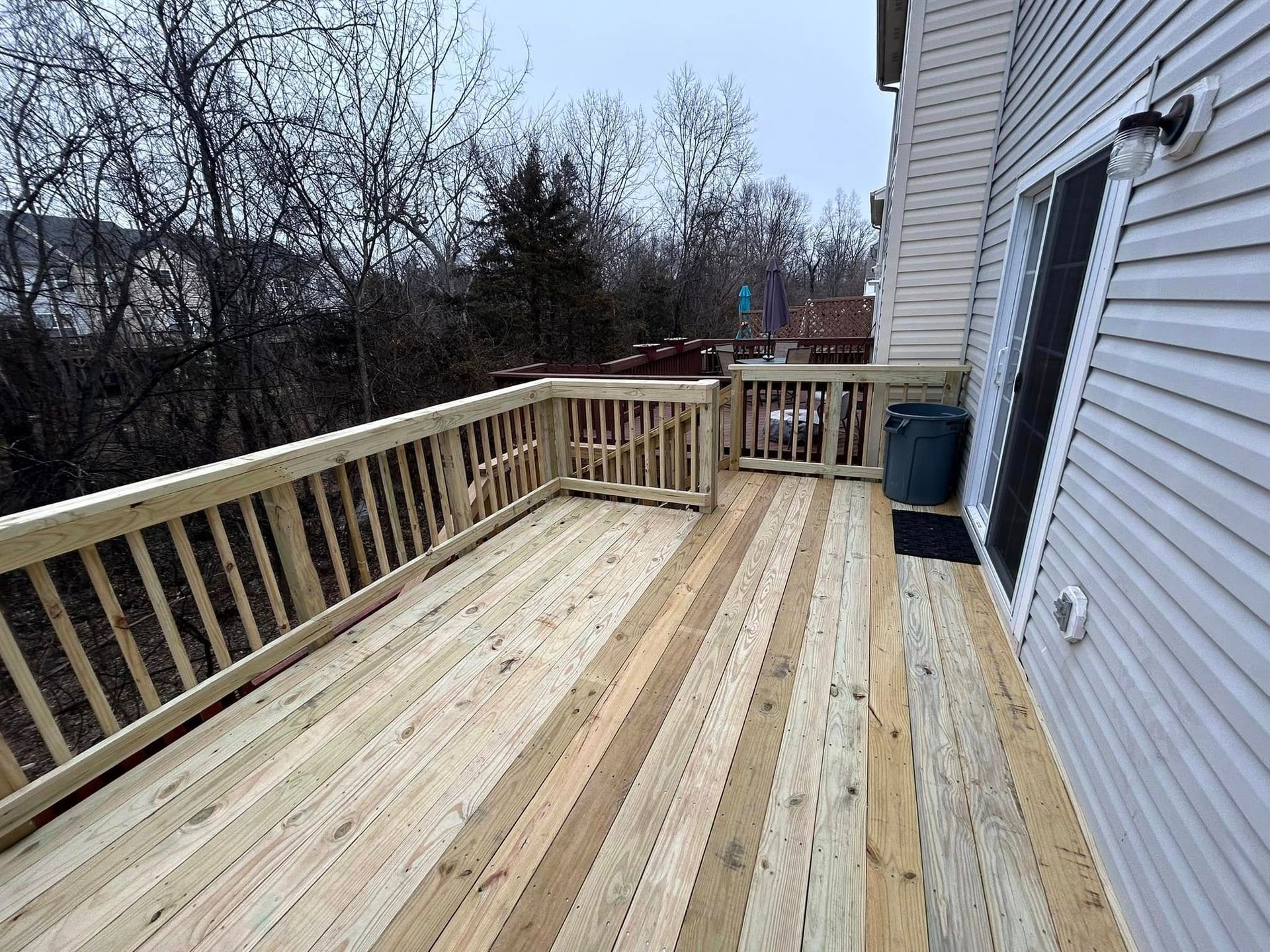 Wooden deck attached to a house, with railings and a sliding glass door.