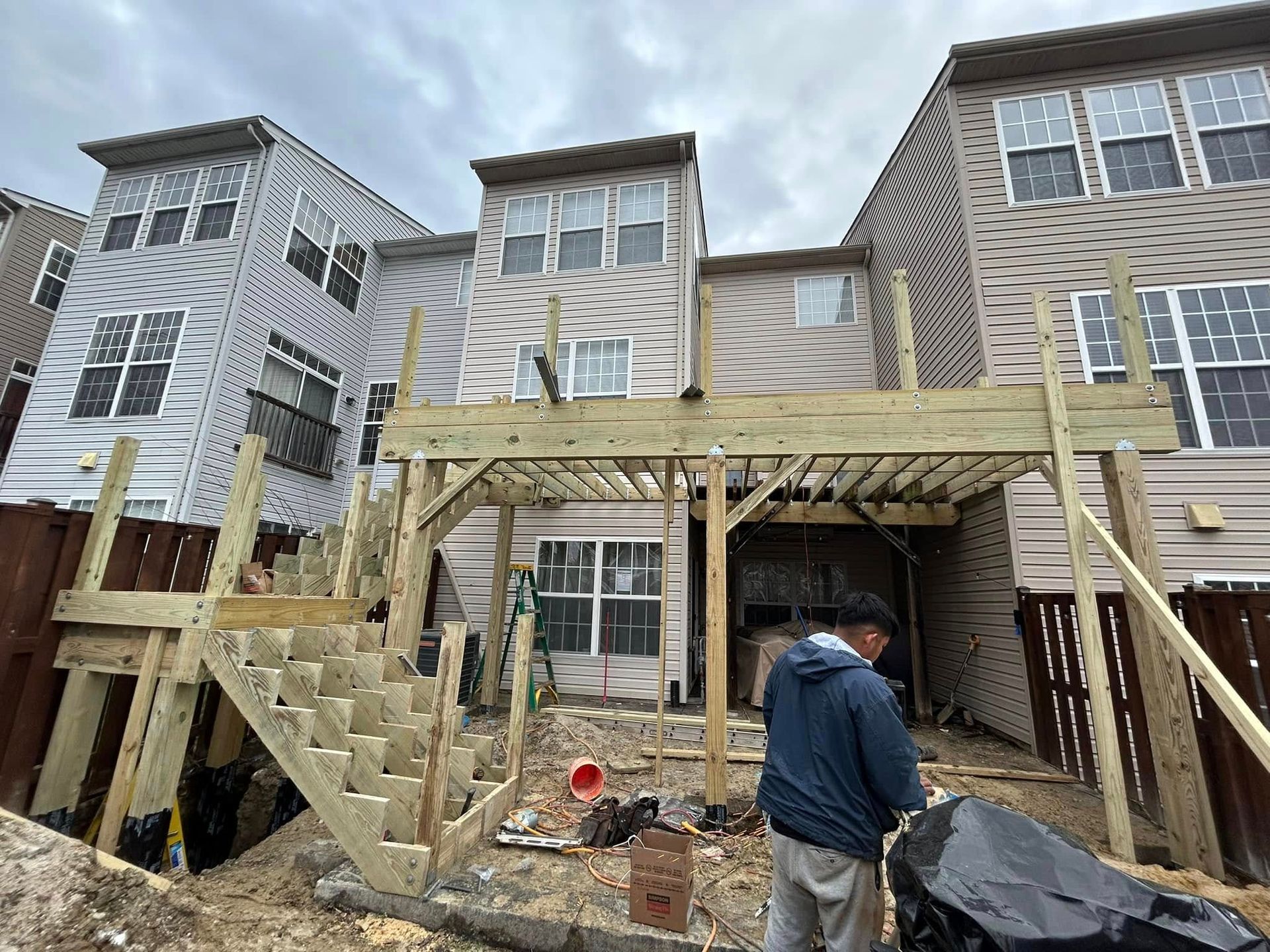 Construction of a wooden deck on the back of a multi-story townhome; worker installs railing.