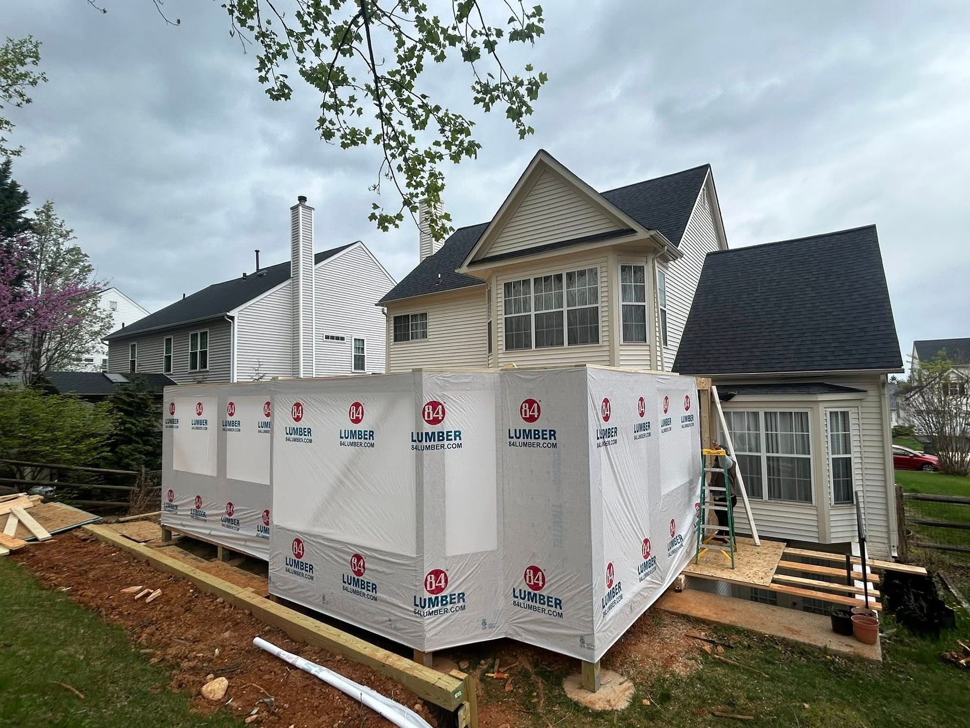 House under construction, deck framed with protective wrap, cloudy sky.