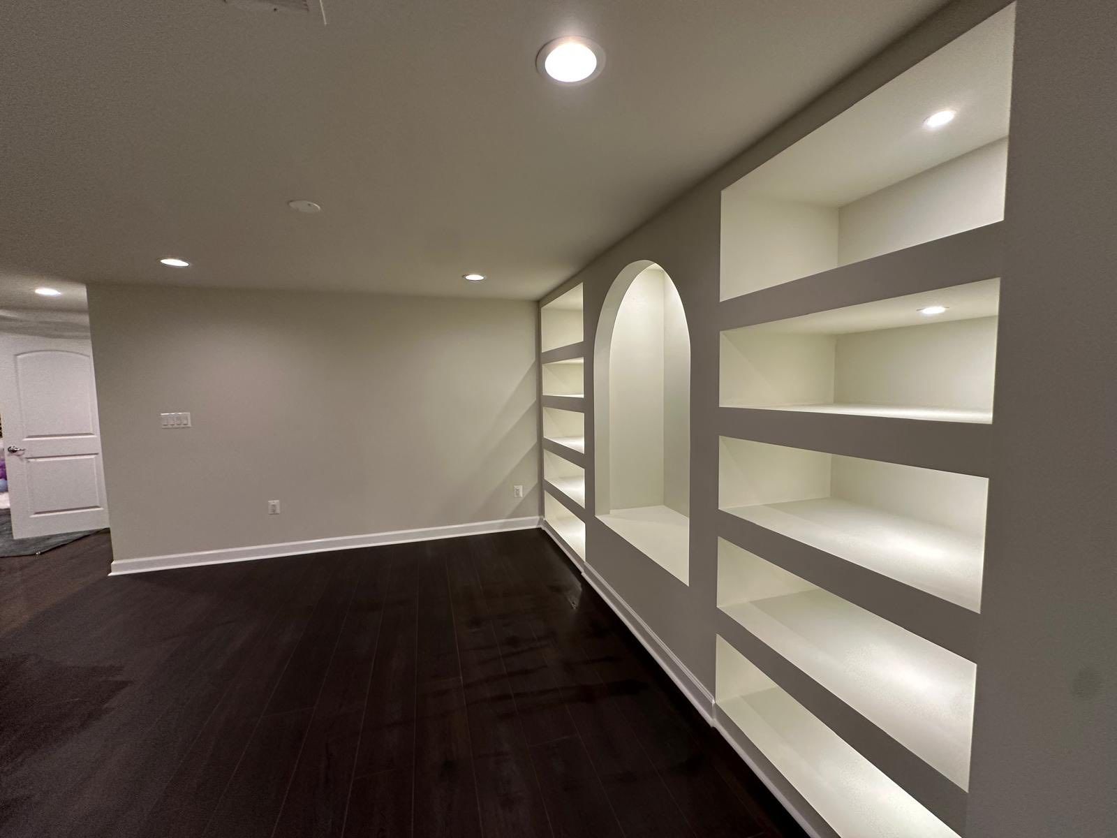 Empty room with dark wood floor, recessed bookshelves lit from within, and a curved niche.