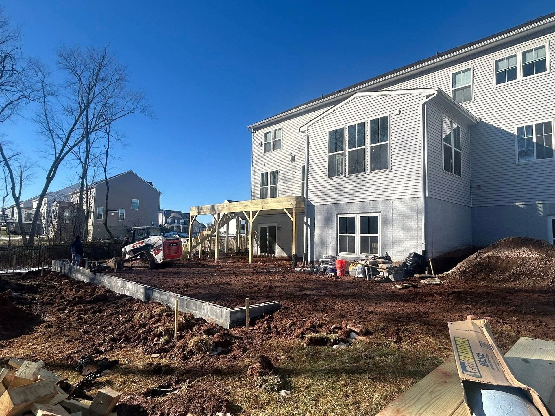 Backyard construction site; wooden deck, house, dirt, and construction materials.