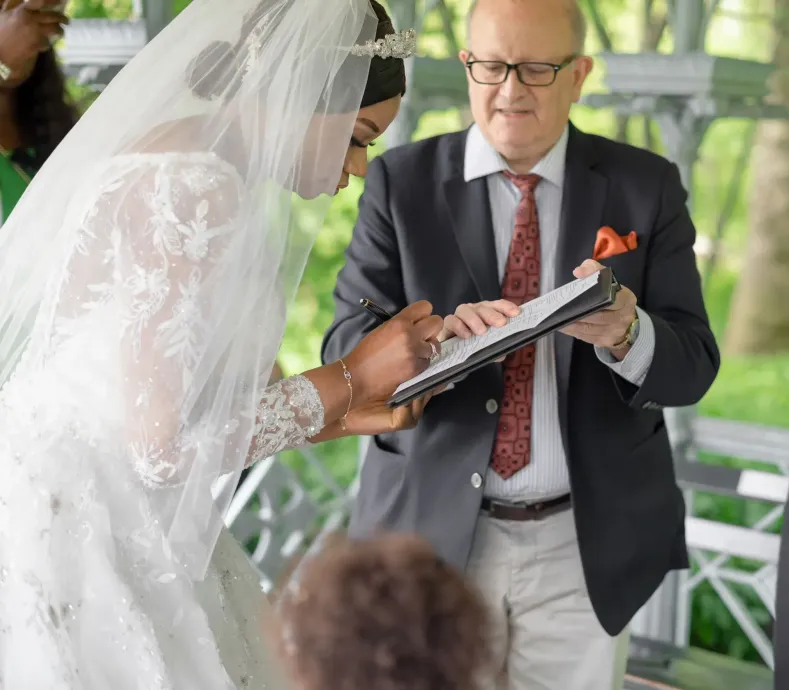 Bride and officiant signing a wedding certificate under a white canopy