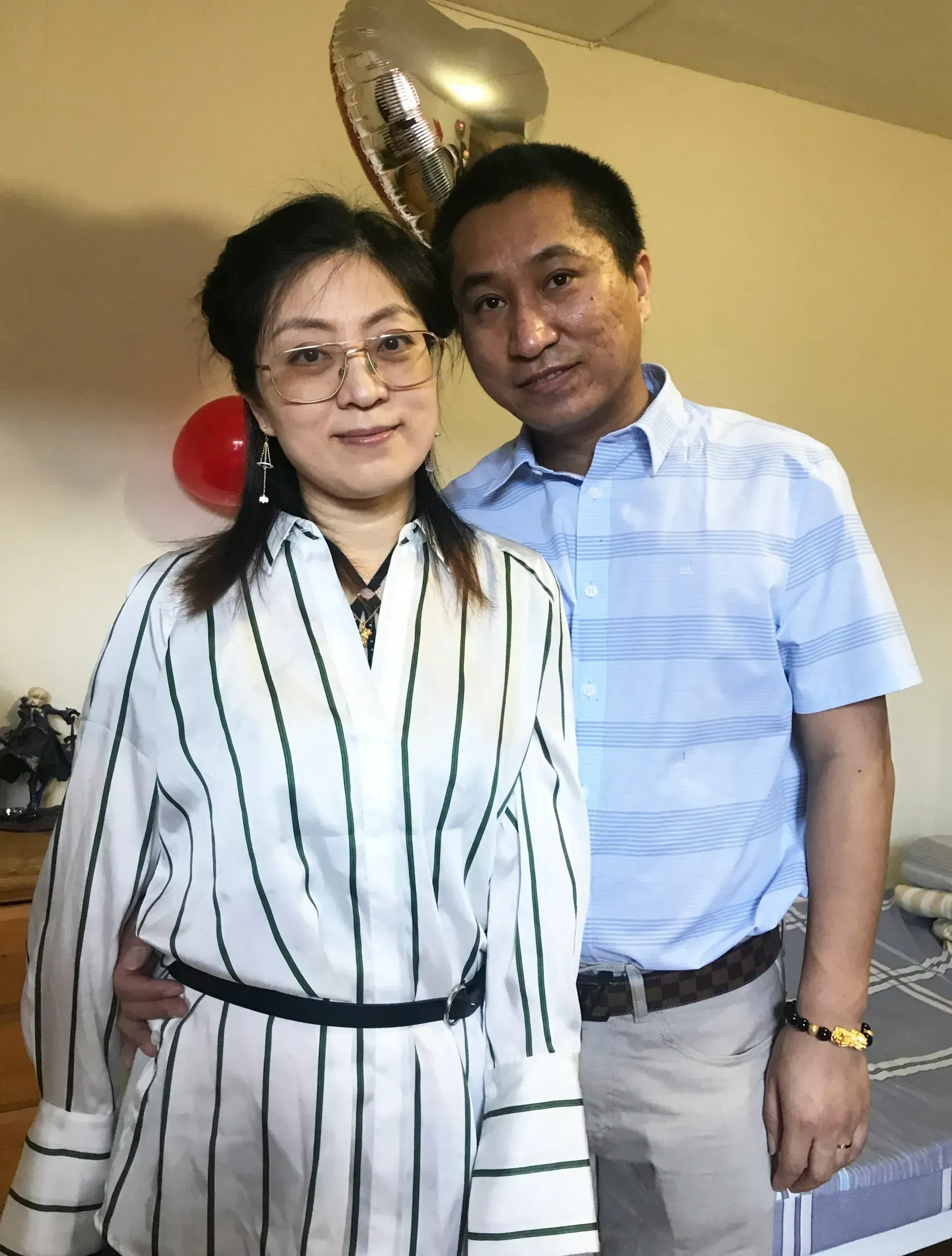 Two people standing indoors, posing beside balloons and a decorated table.