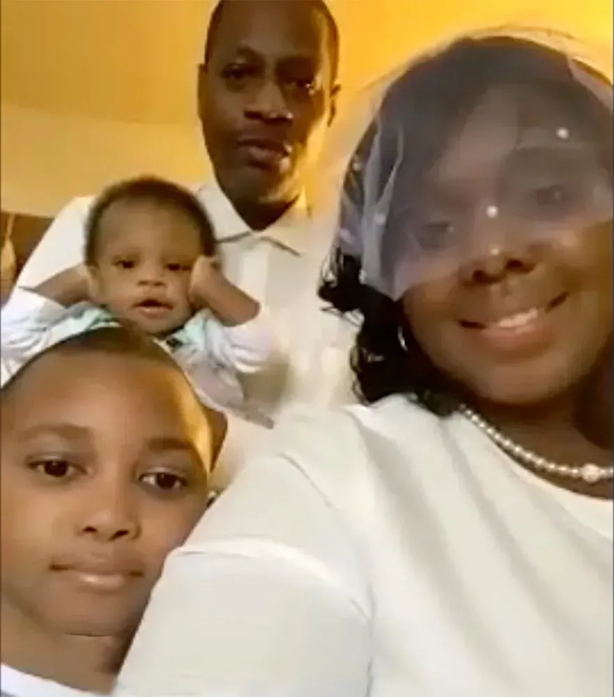 Four people posing closely together indoors, smiling at the camera in white clothing.