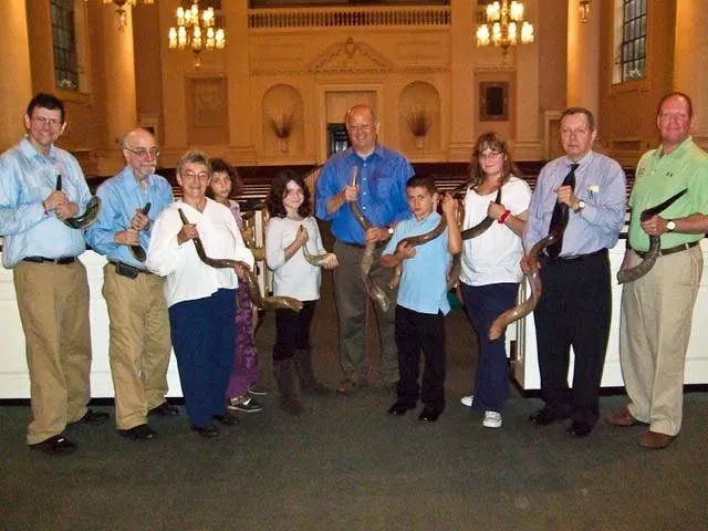 Group of people standing indoors, holding small blue birds in a large hall