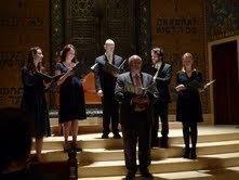 Choir singing on a church stage, holding black folders under warm spotlight