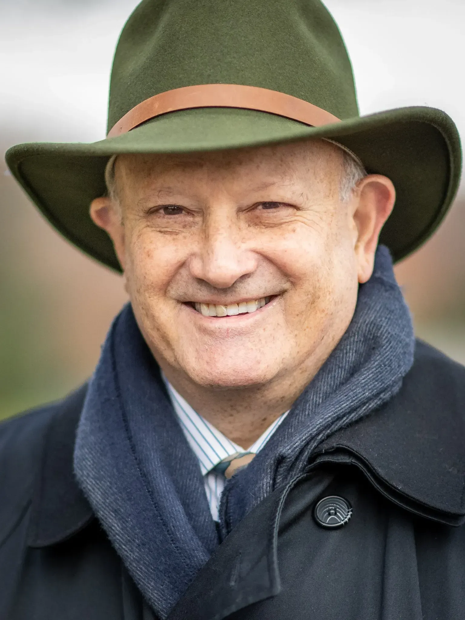 Smiling person in a green hat and dark coat with a navy scarf outdoors