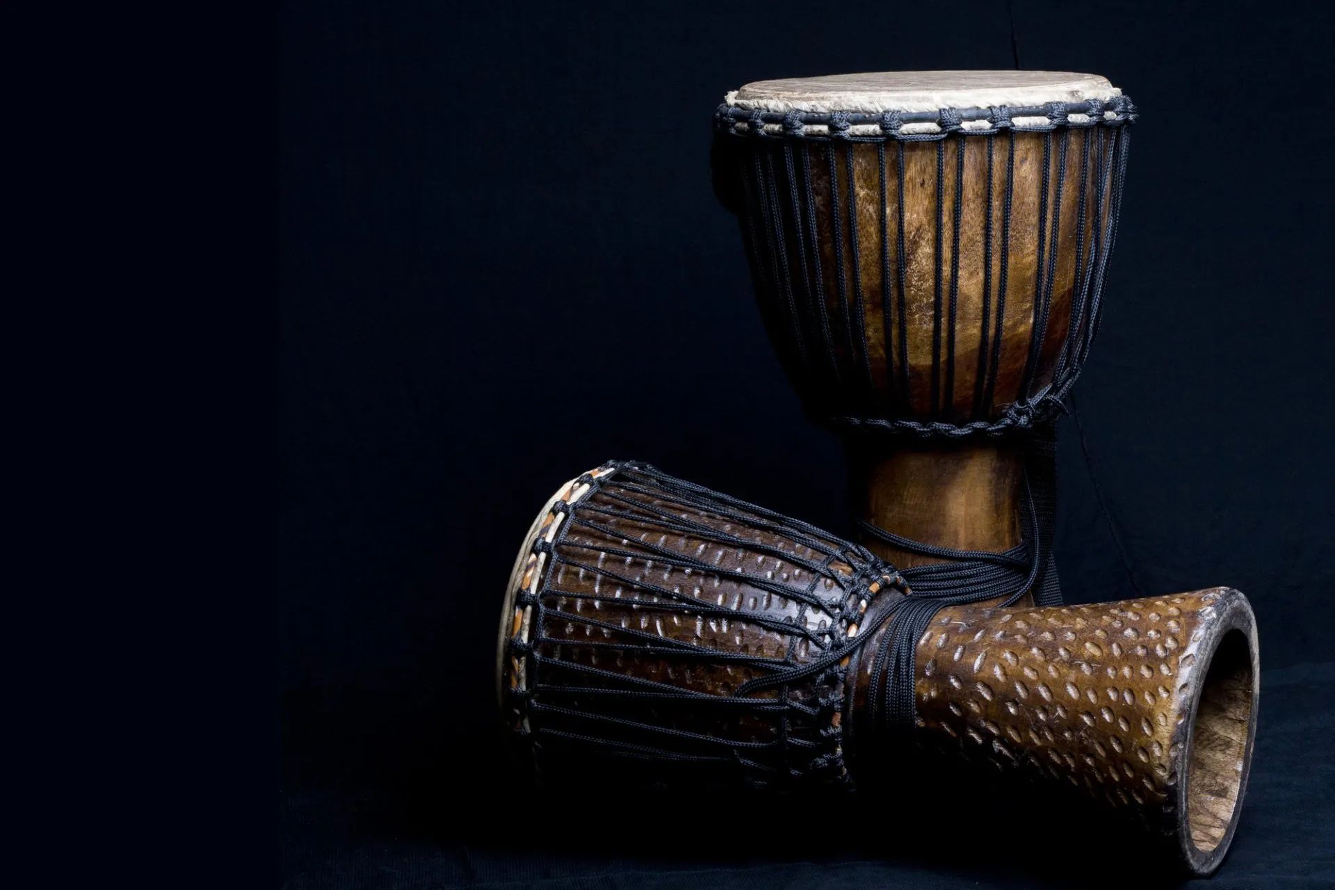 Three wooden hand drums on a dark background, with one upright and two lying on their sides.