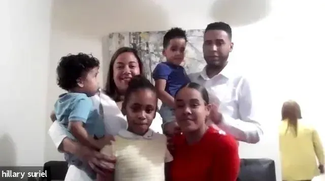 Family of six posing together indoors, with one child held by an adult and everyone facing the camera.