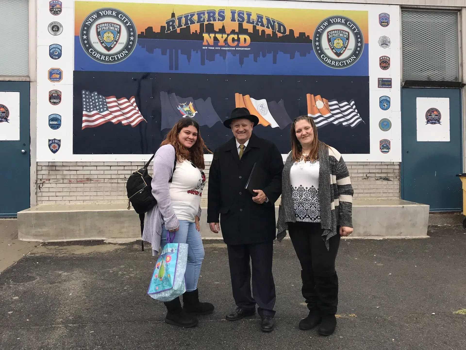 Three people posing in front of a New York City banner with police insignia and American flags.