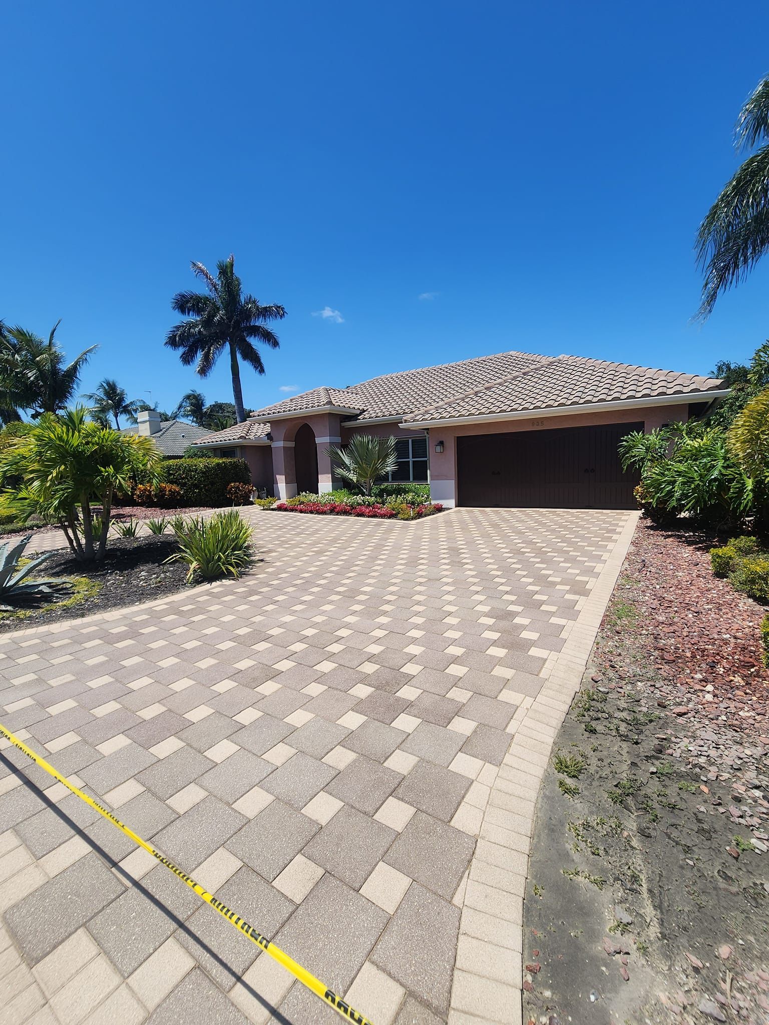 A large house with a brick driveway and a palm tree in the background.