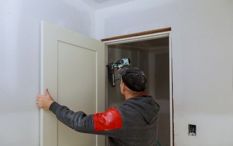 home remodeling carpenter working on door installation with drill power tool, installing hinges.