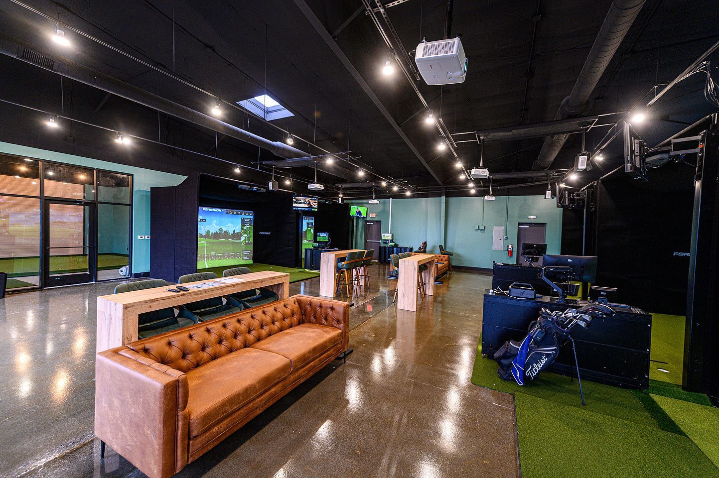 Modern office lounge with leather couch, gaming area, and polished floor under hanging lights