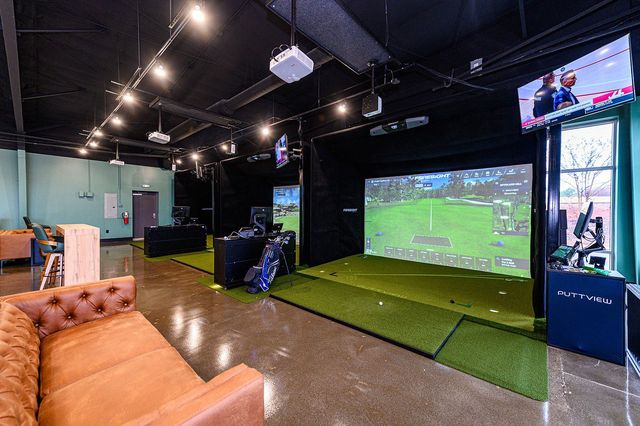 Indoor gaming lounge with a large projected soccer game on a turf wall and a tan couch in front