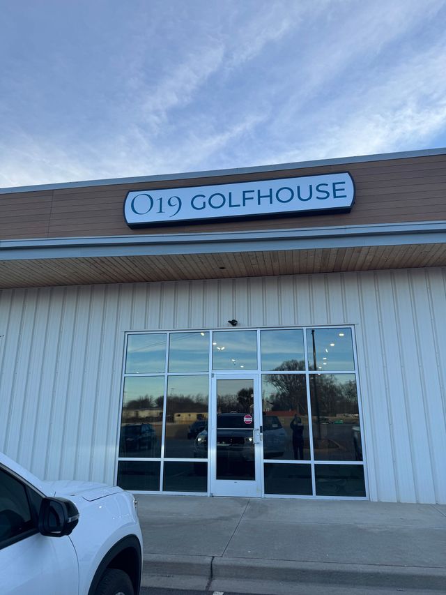Golfhouse storefront with glass doors and beige siding under a tiled roof, blue sign above the entrance