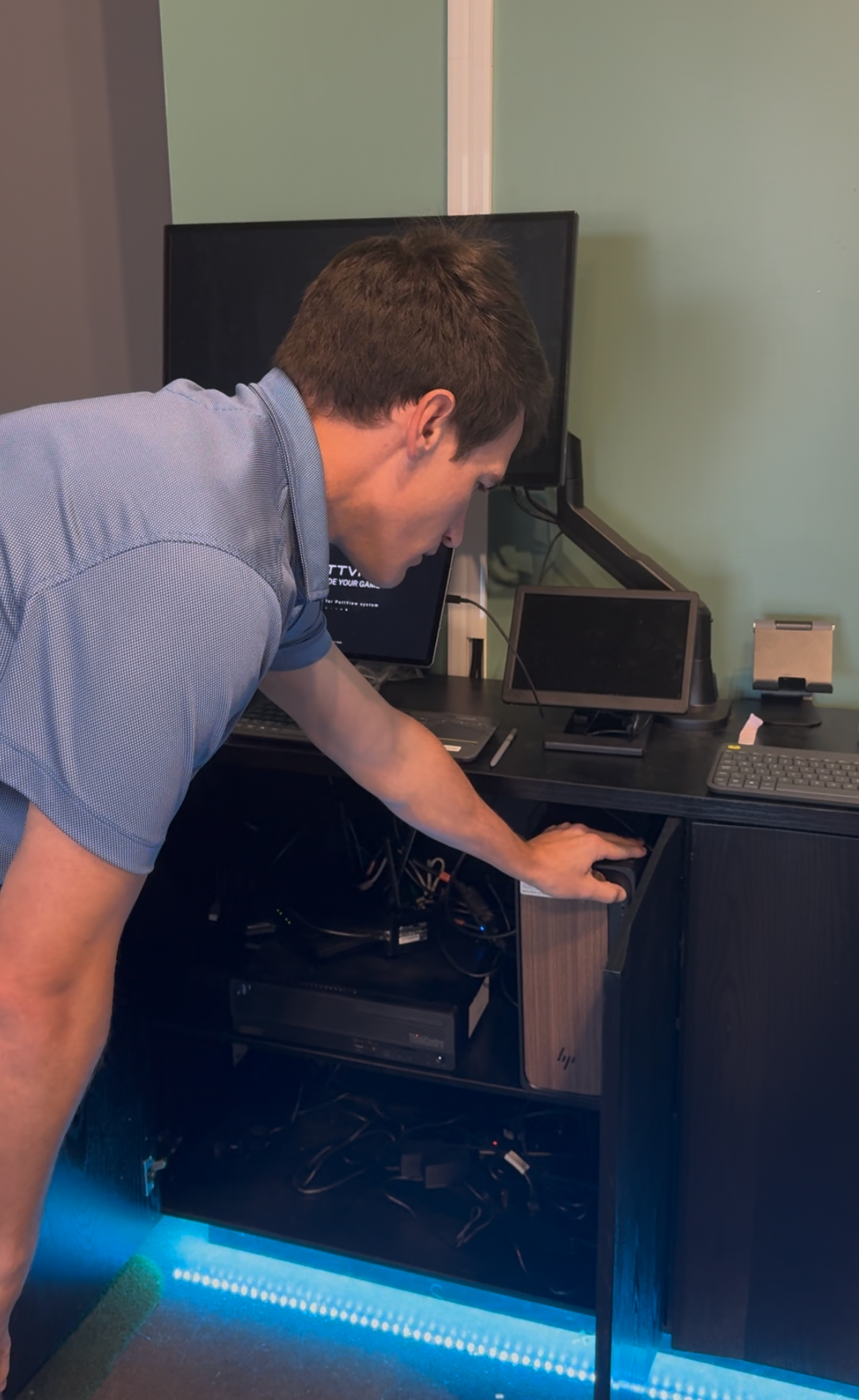 Person leaning into an open desktop computer tower, reaching inside in a dim room.