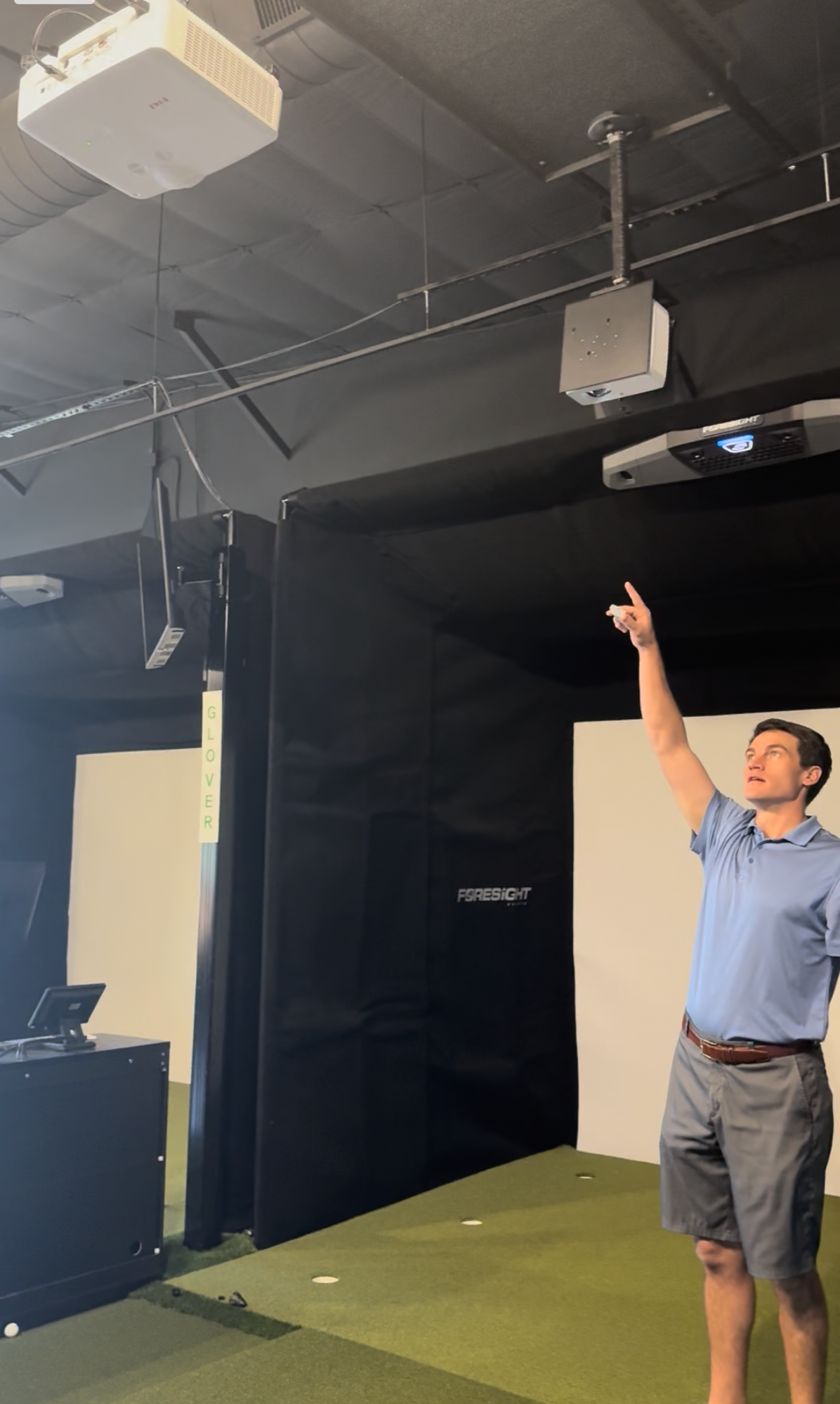 Man pointing upward in a studio gym with hanging ceiling equipment and dark walls