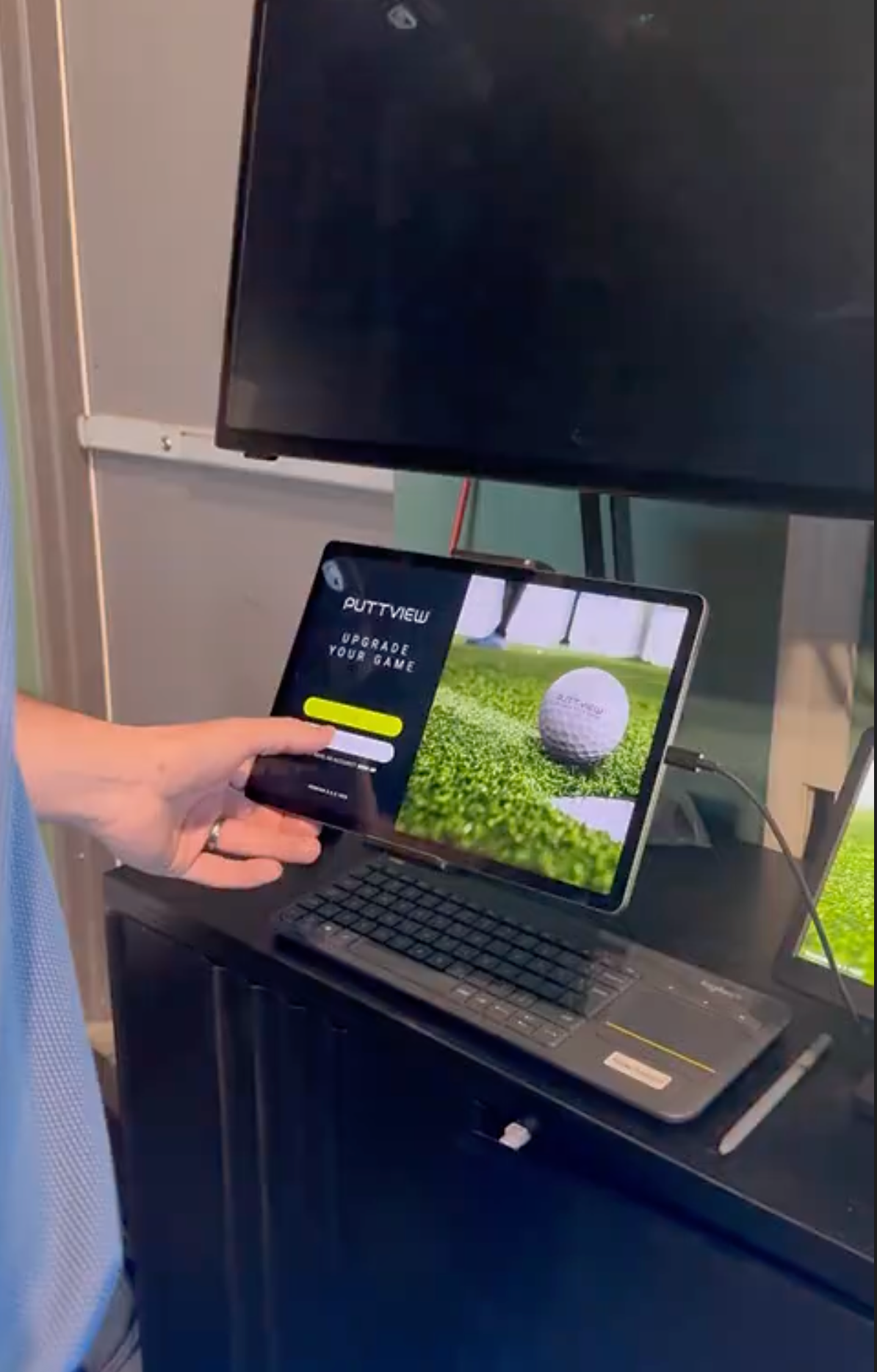 Hand holding a smartphone beside a laptop showing a golf course app on a desk
