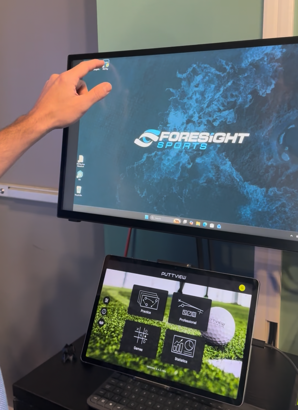 Hand pointing at a monitor showing the Foresight Sports logo above a laptop dashboard