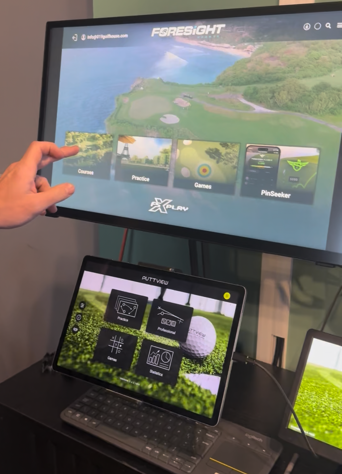 Hand points at a monitor showing a fishing game above a laptop with a tile-based game interface