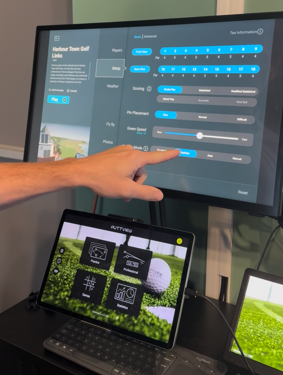 Person adjusting TV settings on a screen above a laptop with a golf game displayed below.