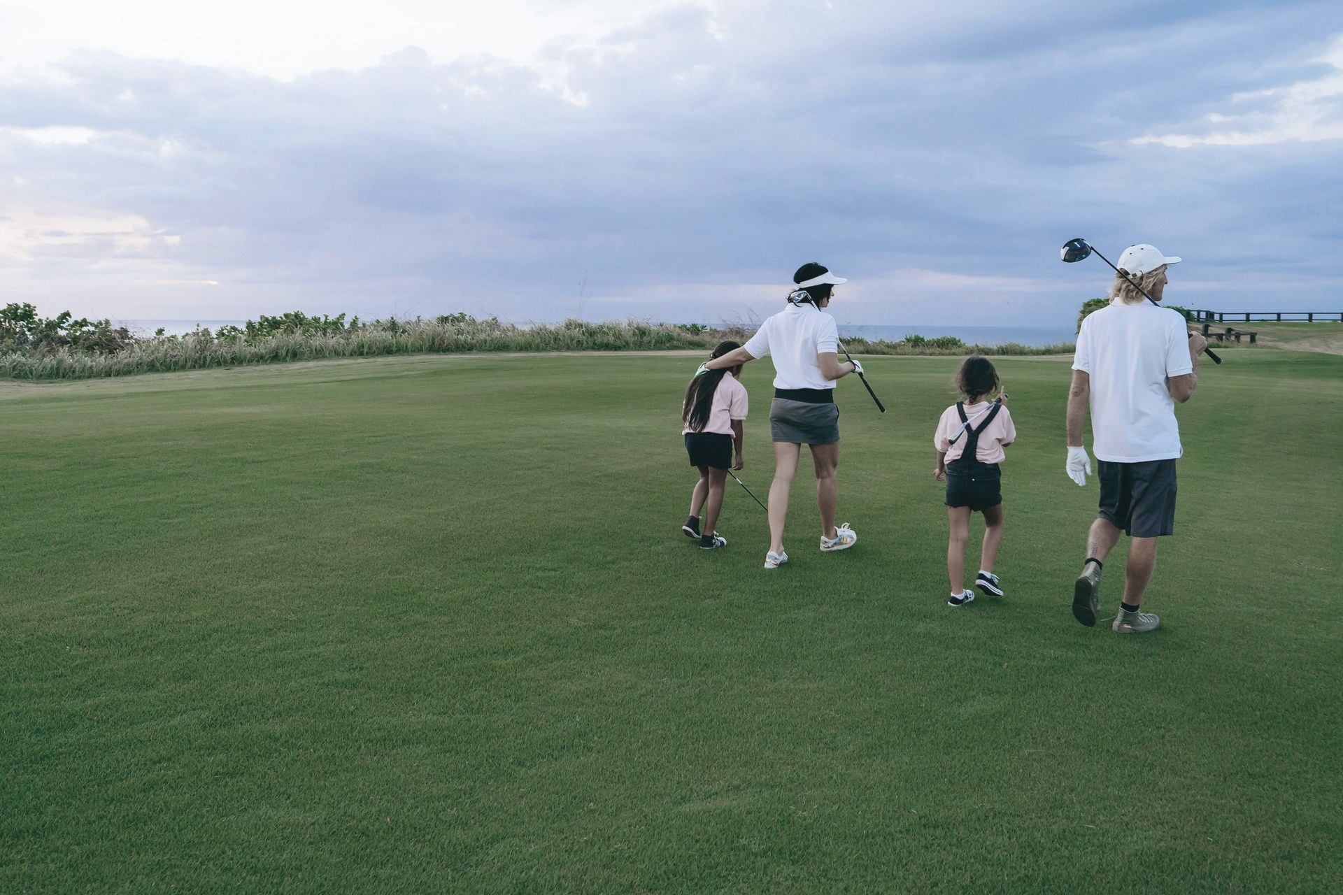Four people walking across a grassy golf course under a cloudy sky