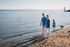 Two adults and two children walking along a sandy beach beside calm water