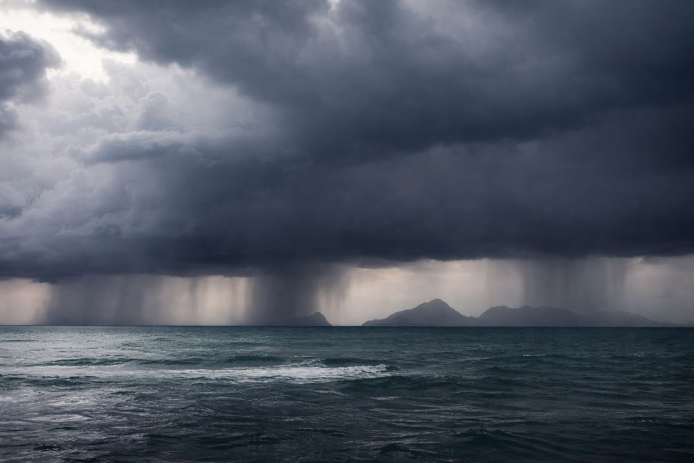 Dark storm clouds over the ocean with rain shafts and a distant island on the horizon