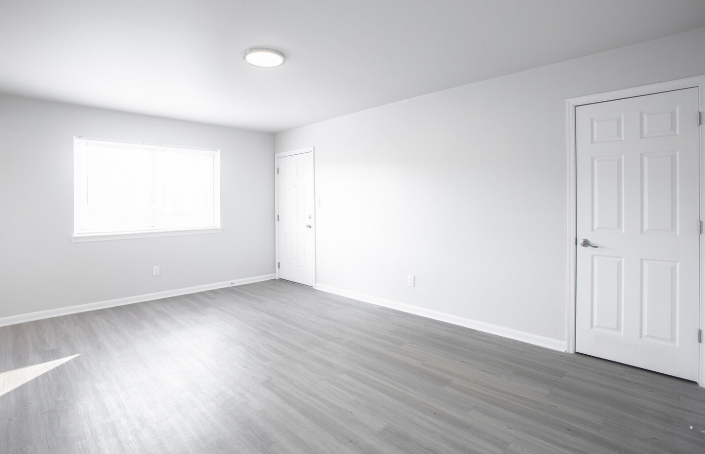 An empty room with hardwood floors , white walls , and a window.