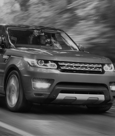 A black and white photo of a range rover sport driving down a road.