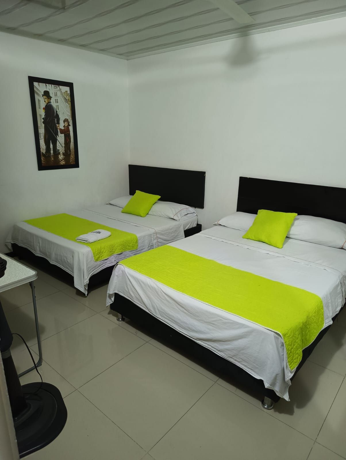 Dos camas individuales con detalles en verde lima en una sencilla habitación de hotel blanca.