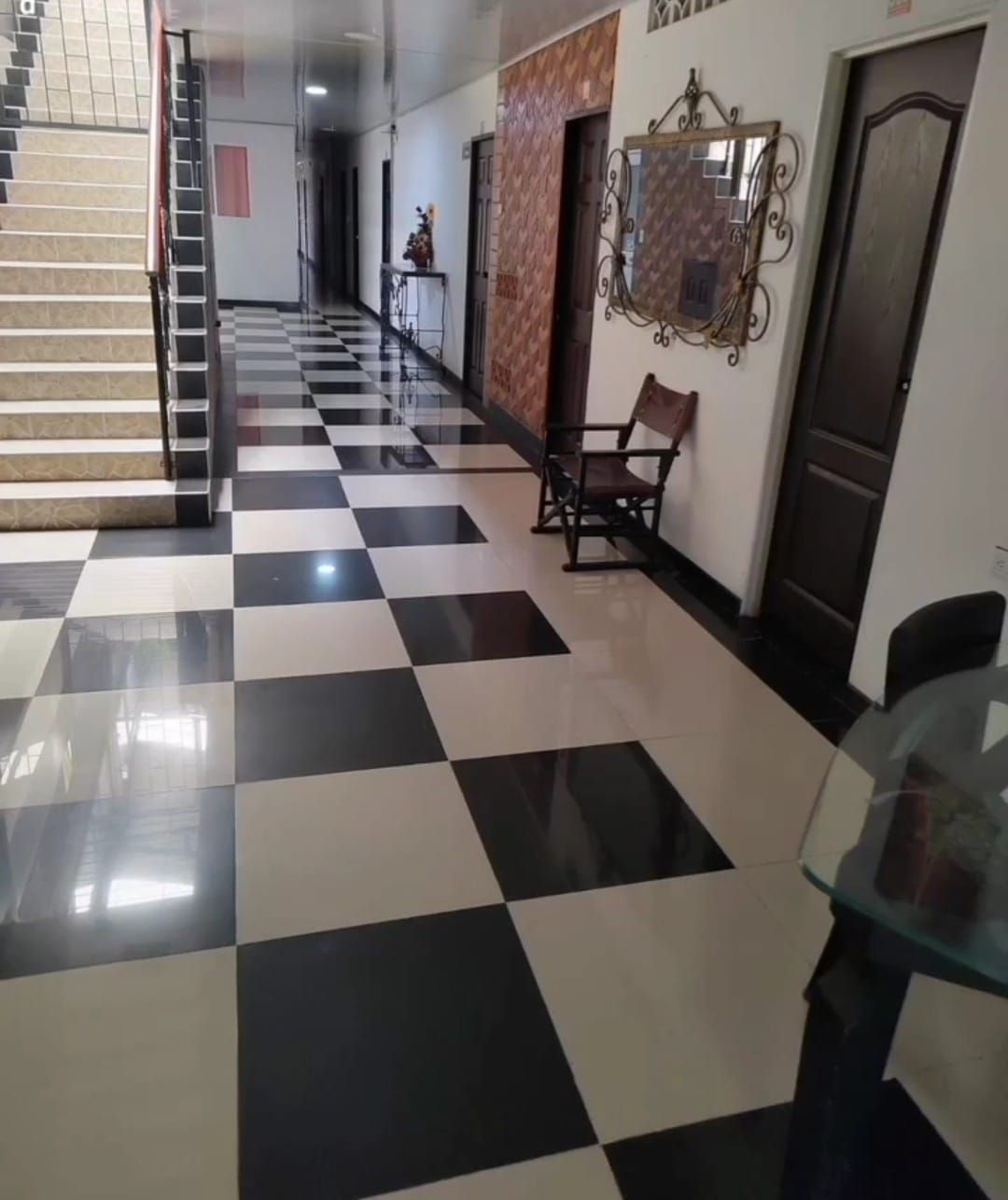 Pasillo con suelo de baldosas a cuadros blancas y negras, escalera, decoración en la pared y sillas a lo largo del lateral.
