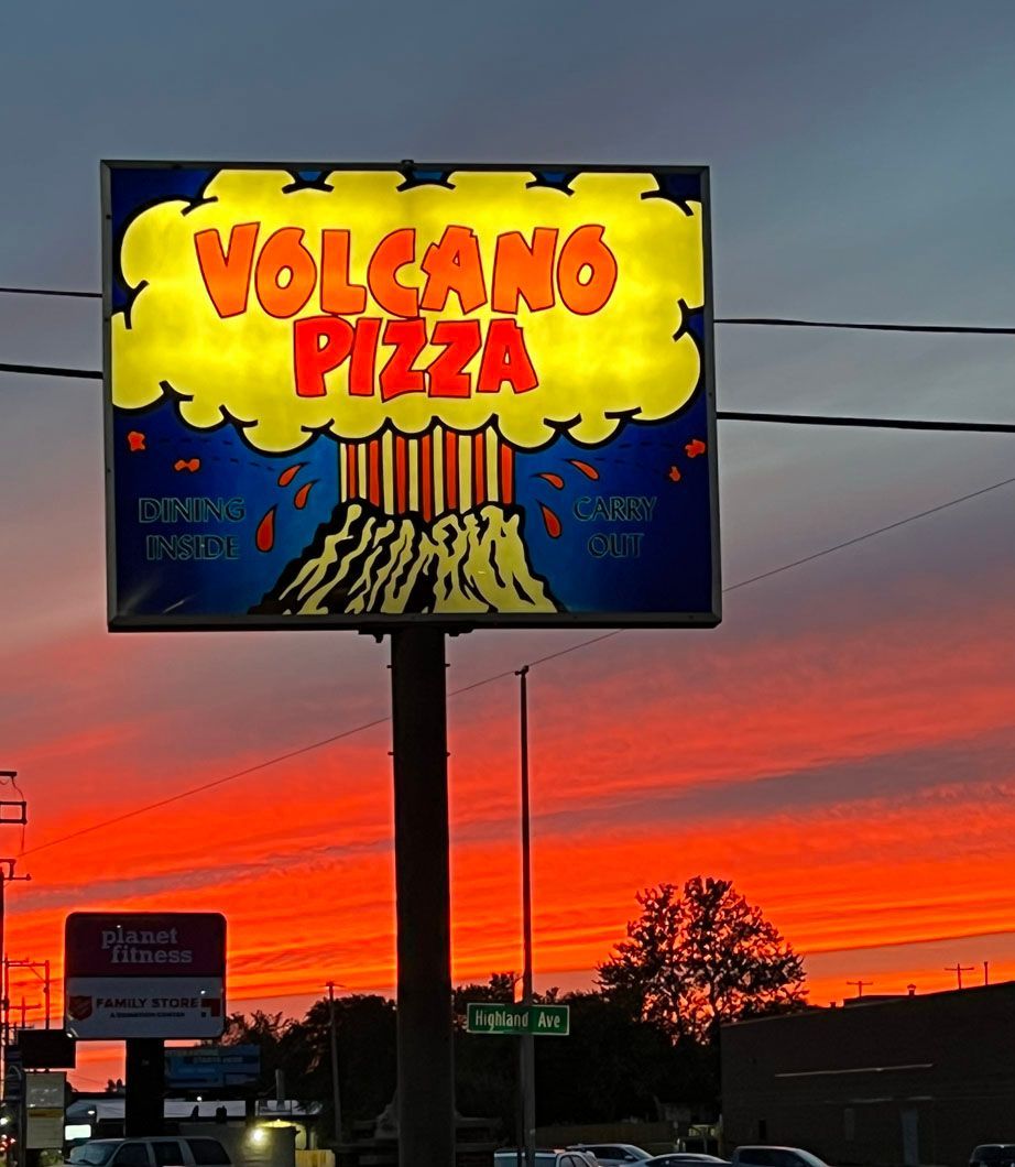 A sign for volcano pizza is lit up at night
