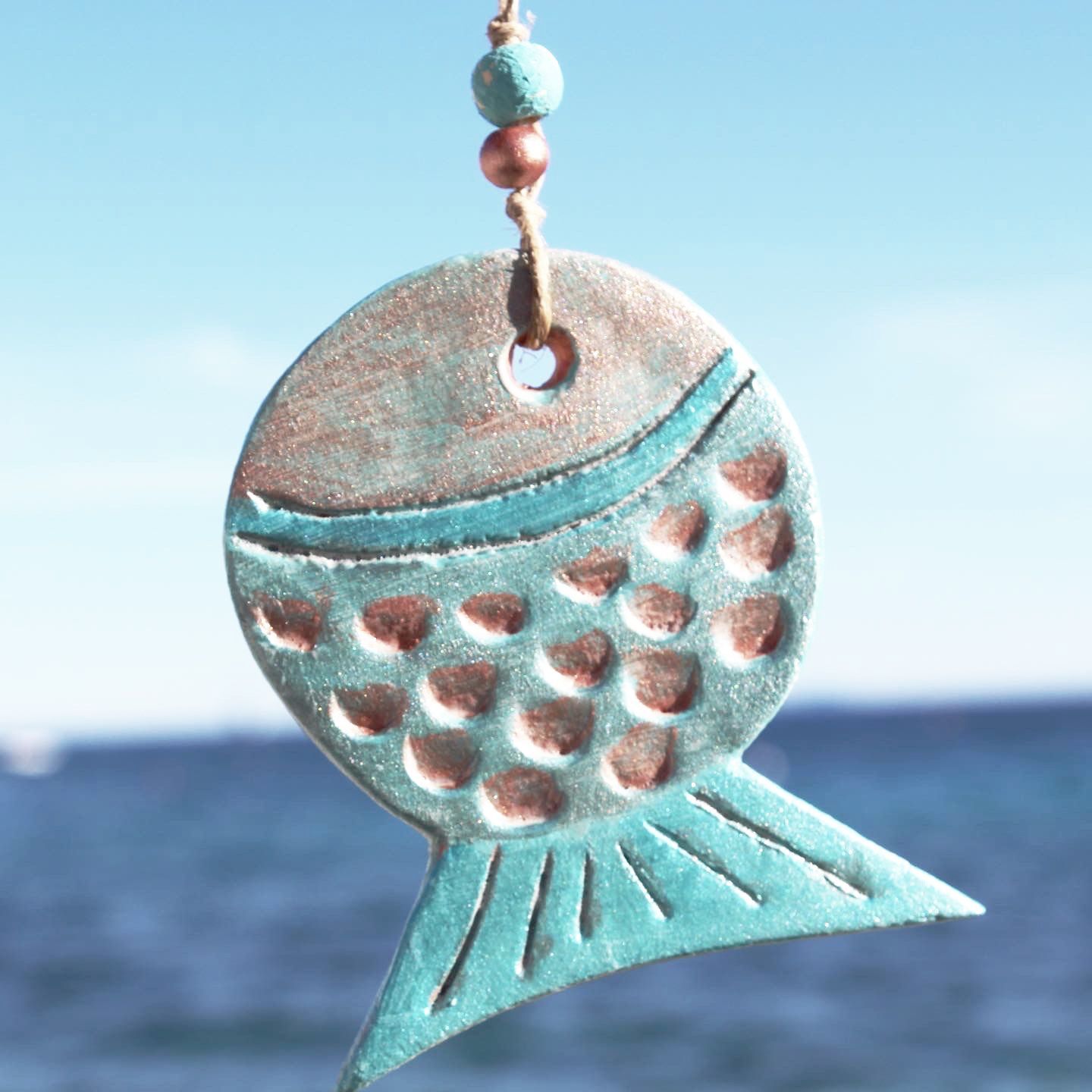 A fish shaped pendant is hanging from a string in front of the ocean
