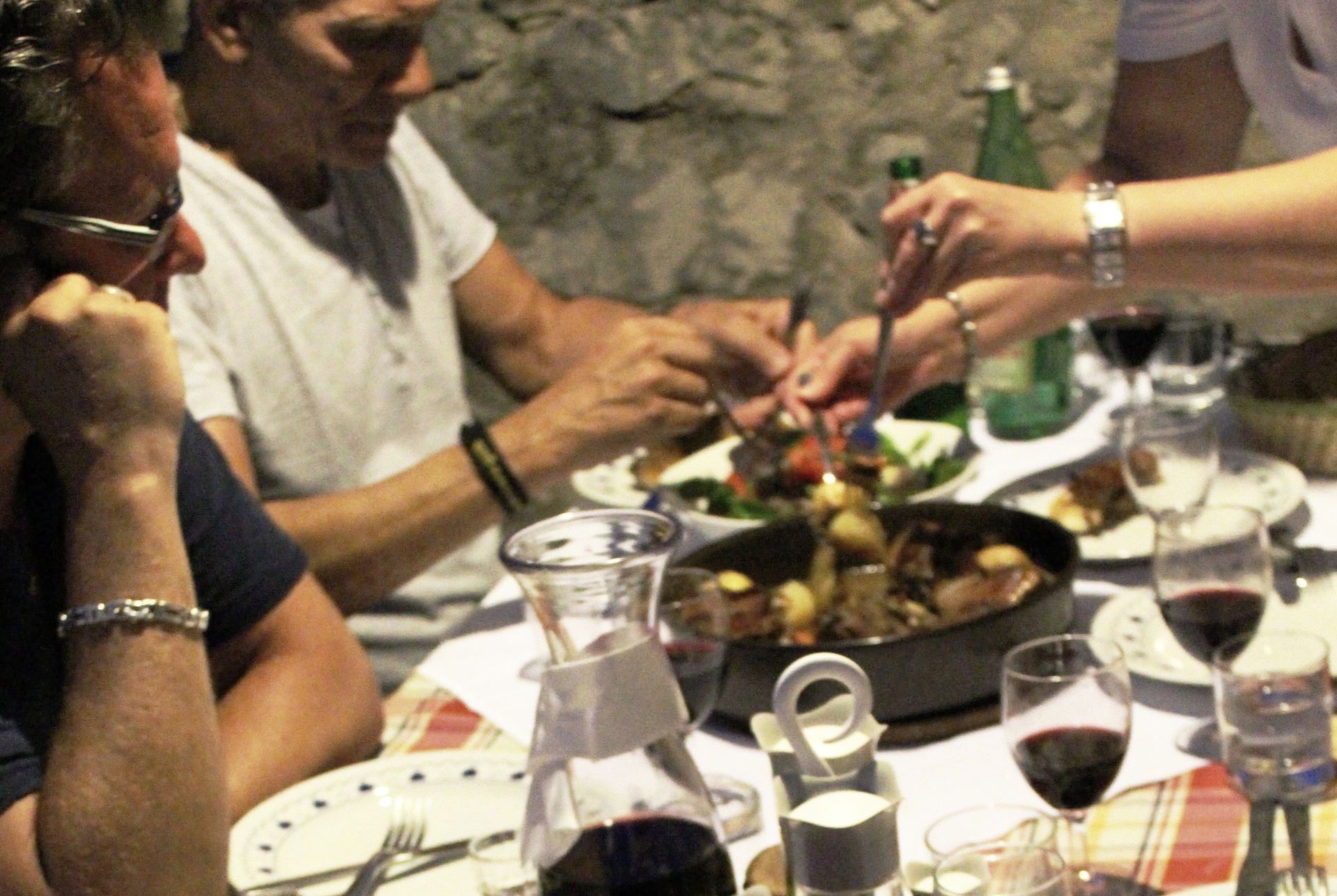 A group of people are sitting at a table eating food and drinking wine.