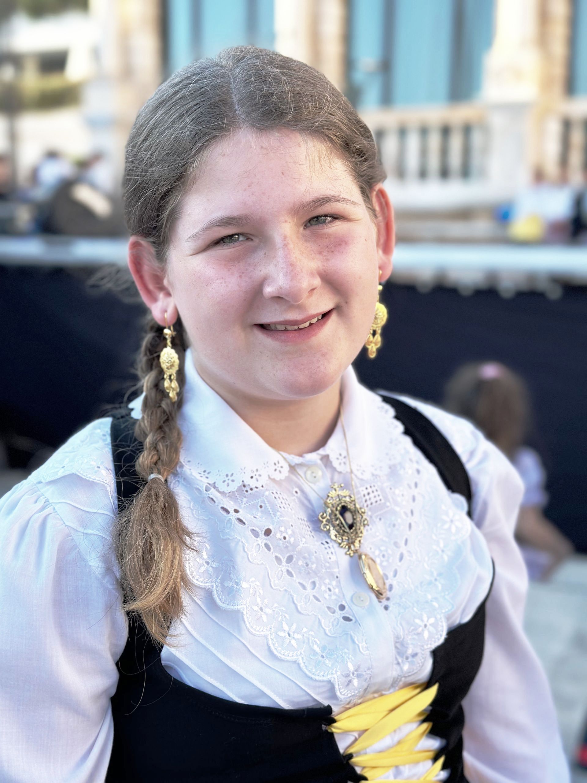 A young girl wearing a white shirt and black vest smiles for the camera