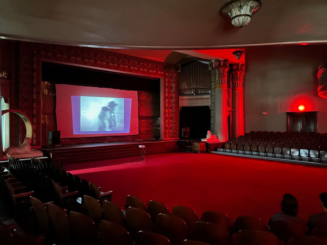 An empty auditorium with red seats and a large screen on the stage.