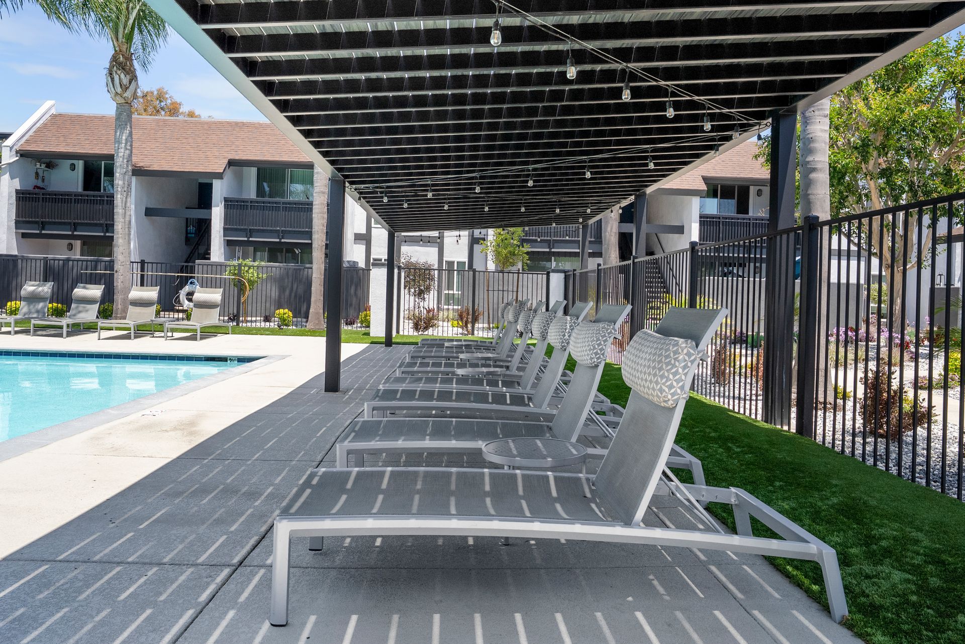 A row of lounge chairs under a canopy next to a swimming pool.