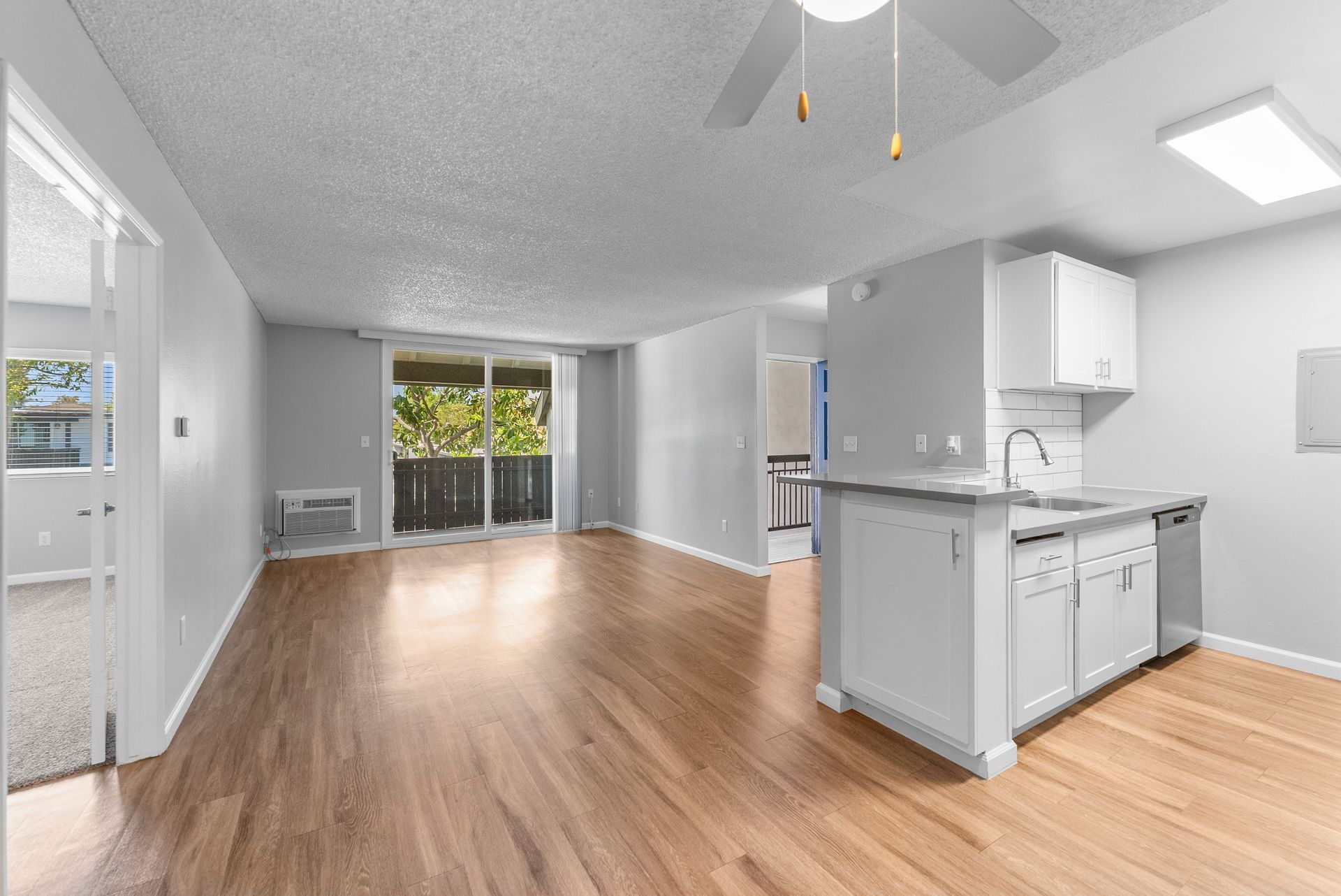 An empty apartment with hardwood floors , white cabinets , and a kitchen.