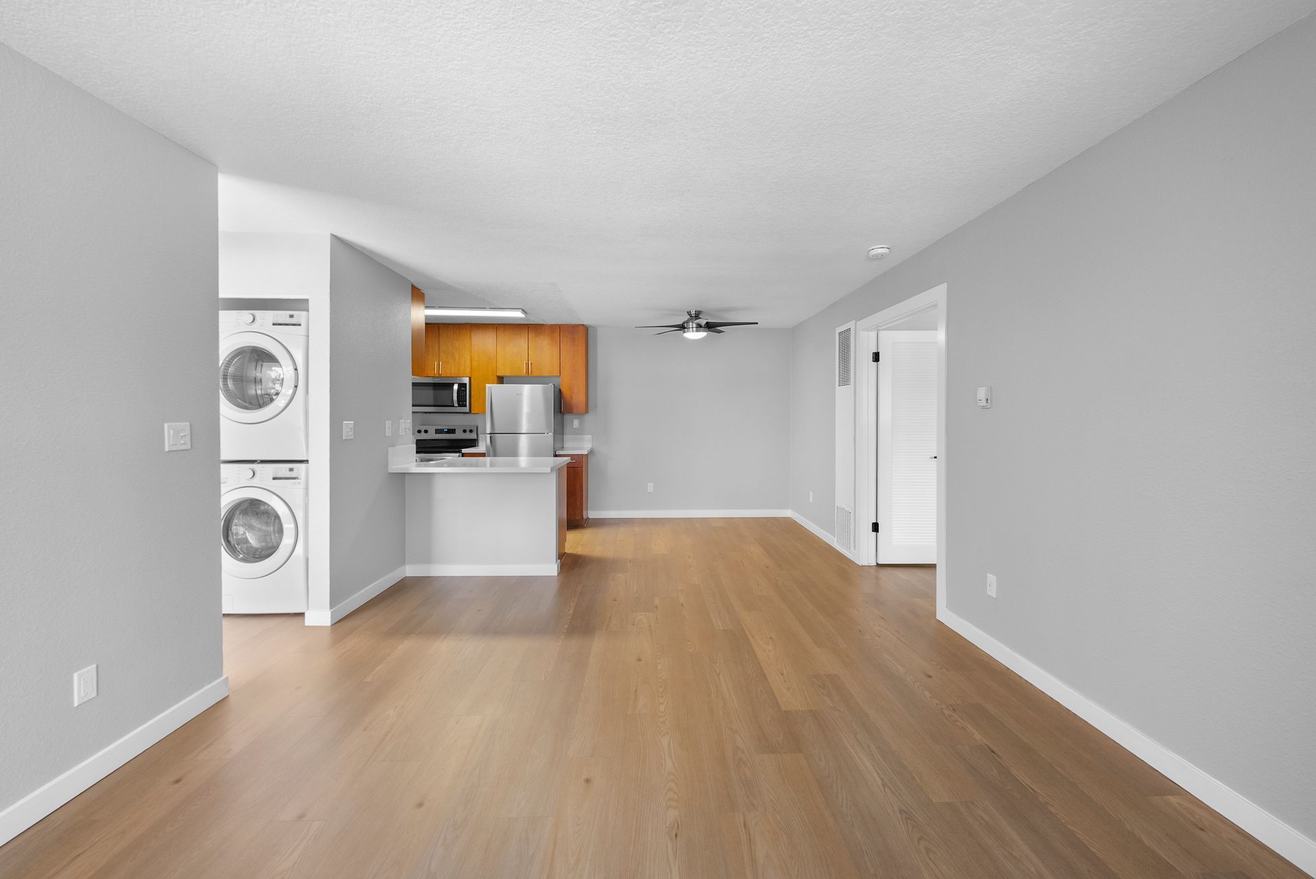 A living room with hardwood floors , a washer and dryer , and a kitchen.