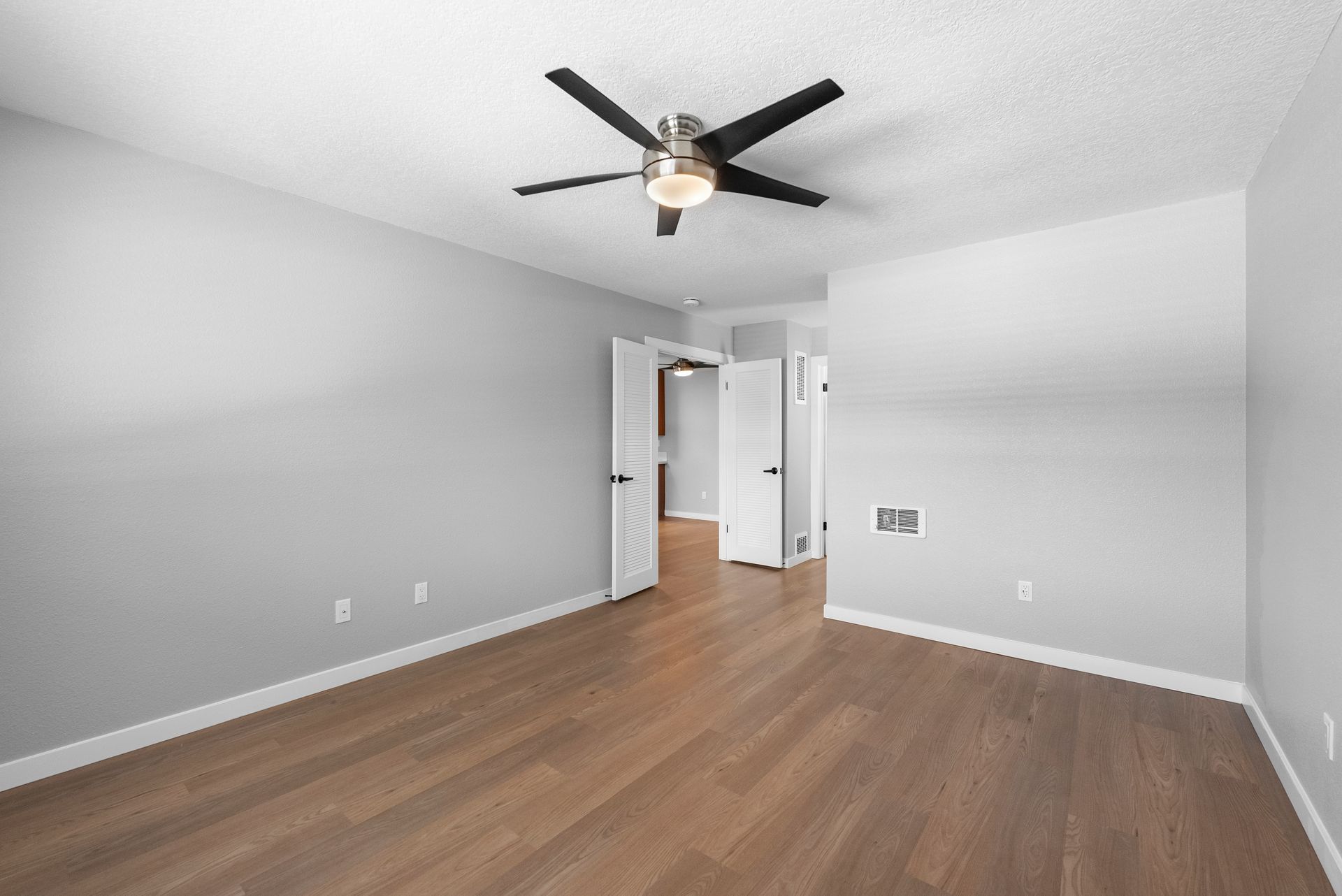 An empty bedroom with hardwood floors and a ceiling fan.