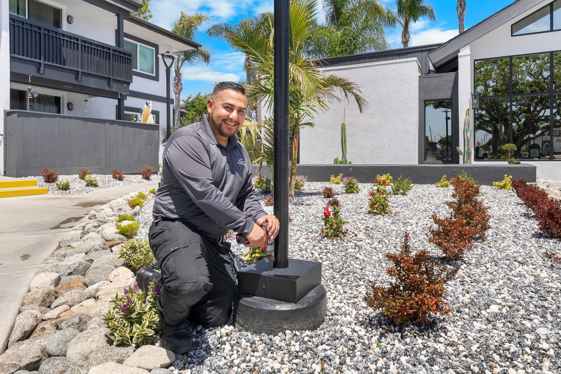 A maintenance man is kneeling down next to a pole in a garden.