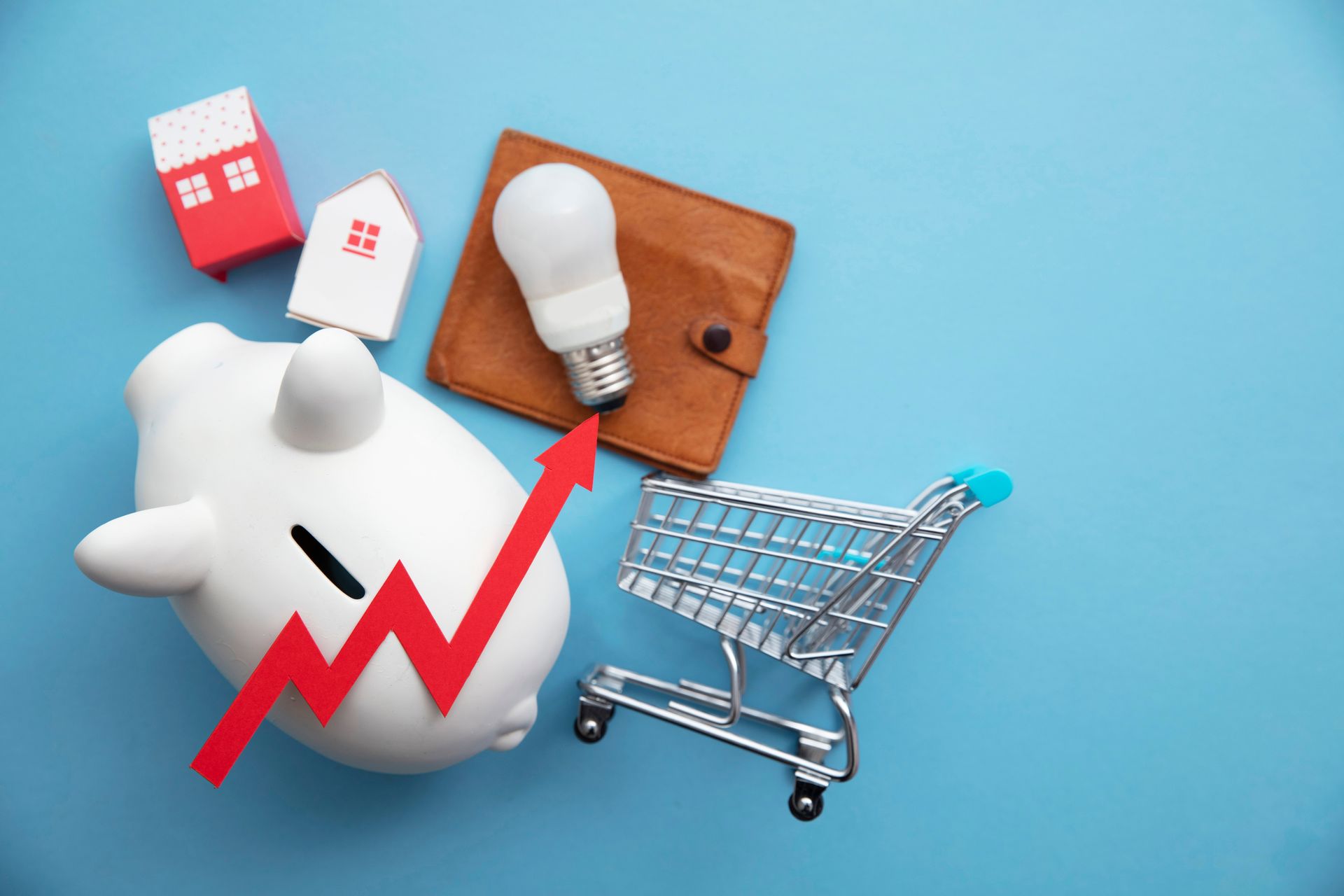 Stock image of a white piggy bank, shopping card, light bulb, stocks arrow pointing up, wallet, paper house