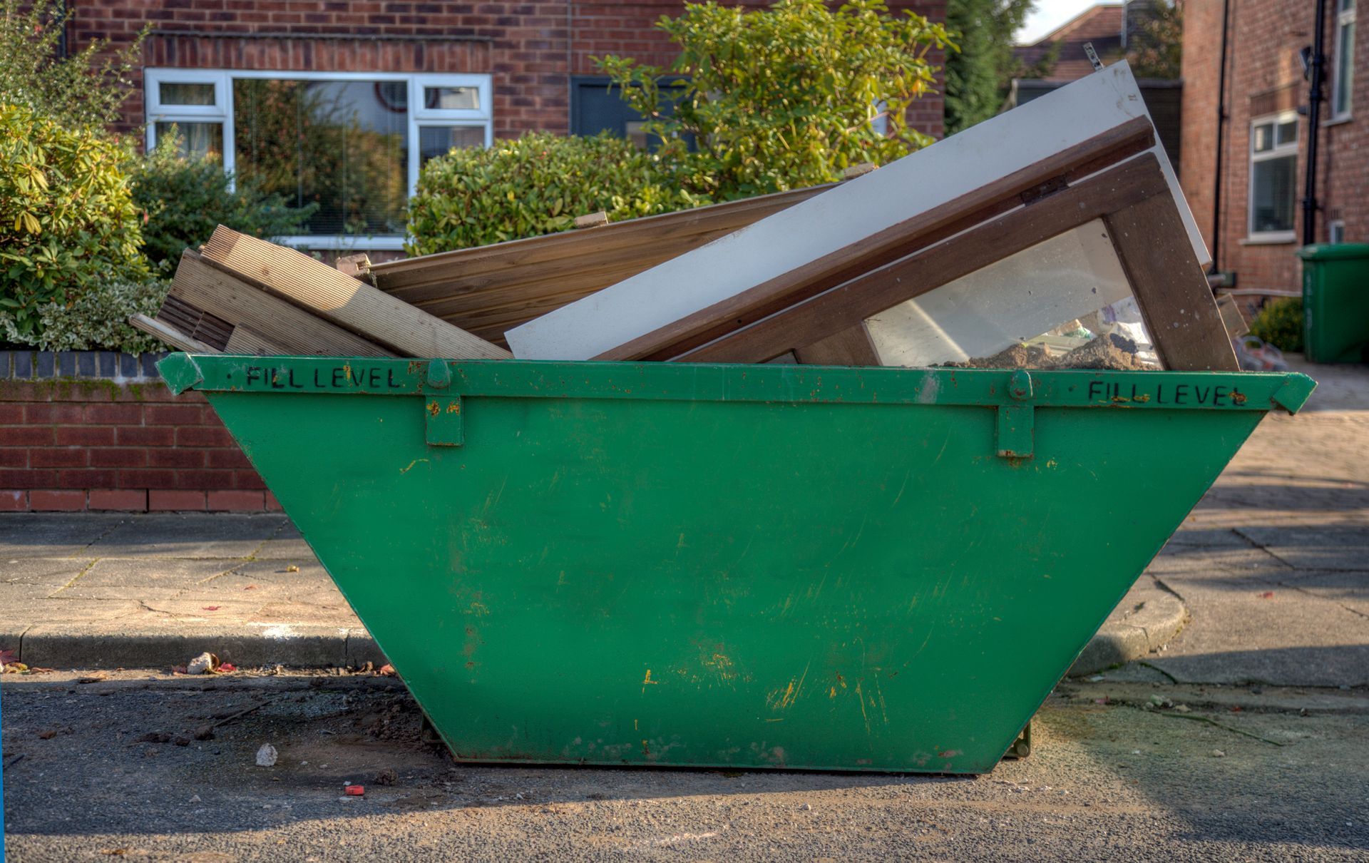 Green garbage receptacle overflowing with construction debris, including wood and windows, parked on