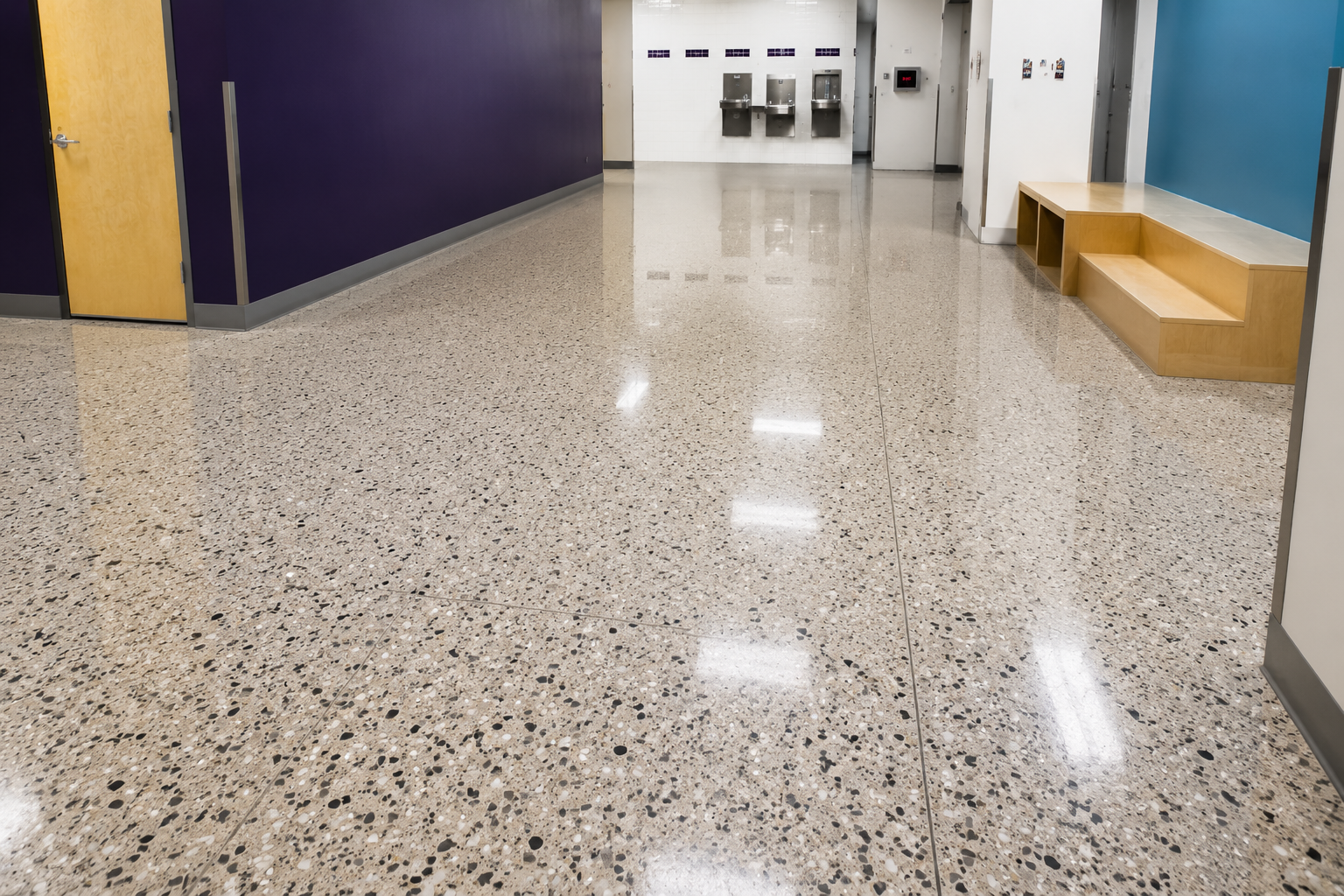 Person in blue jacket and jeans spreading gray sealant on a floor with a tool.