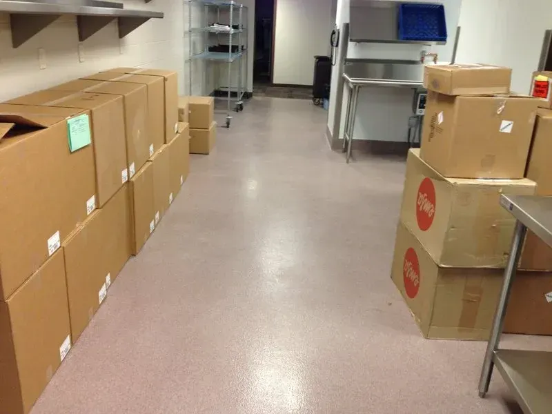 Storeroom aisle with stacked cardboard boxes on both sides and metal carts at the back.
