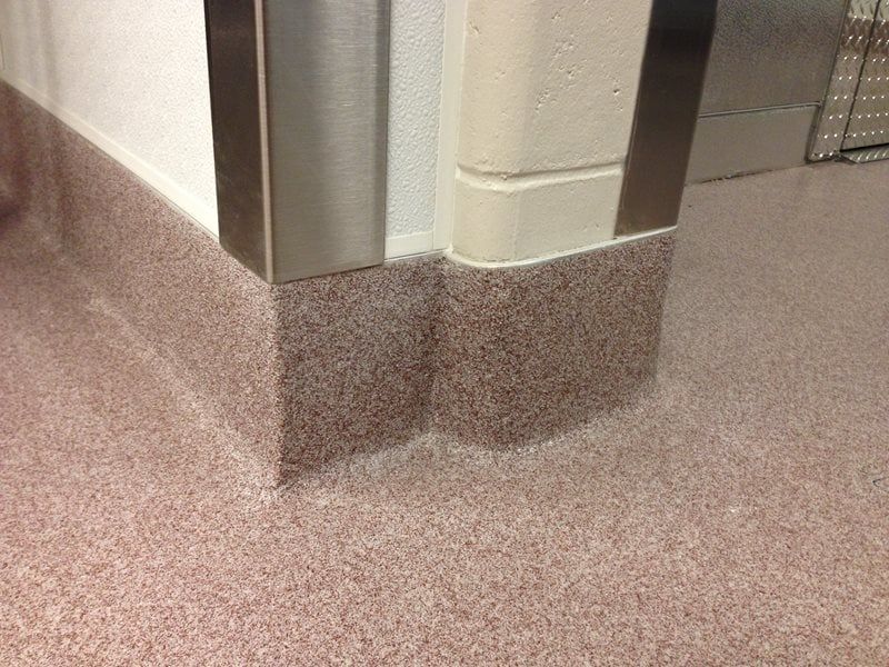 Corner of a hallway with beige walls and a speckled brown floor trim.