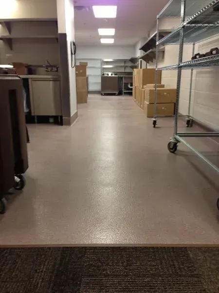 Empty storage room with shelves, boxes, and metal carts under fluorescent lights.