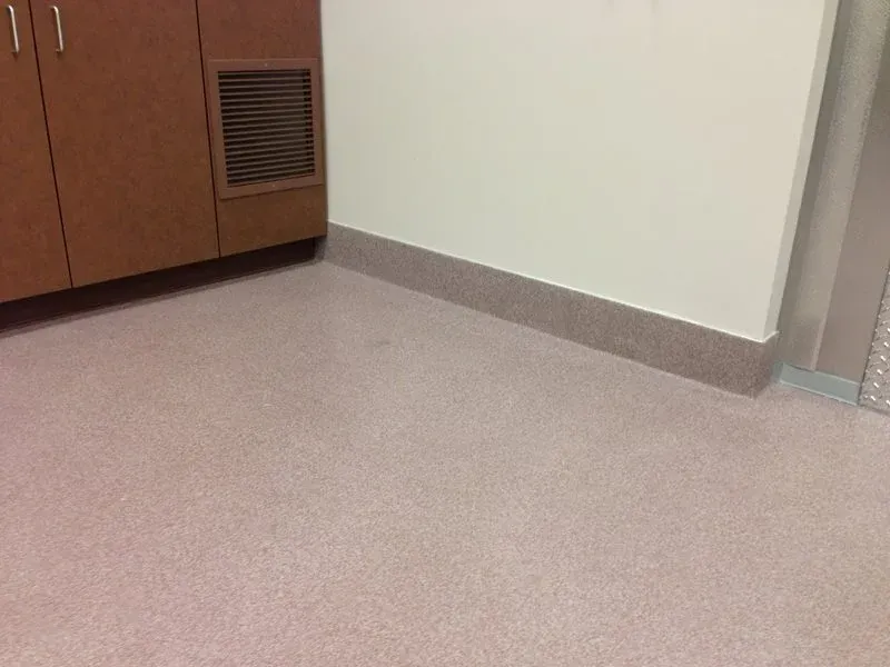 Empty office corner with beige carpet, white wall, and wooden cabinet with vented panel